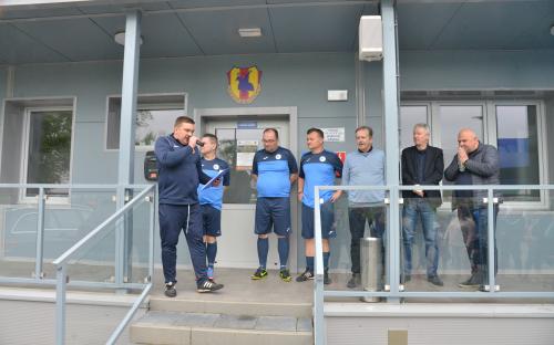 Zdjęcie nr 1: grupa siedmiu mężczyzn stojących przed budynkiem, jeden z mężczyzn trzyma mikrofon, trzech mężczyzn jest w niebiesko-granatowych strojach do gry w piłkę nożną