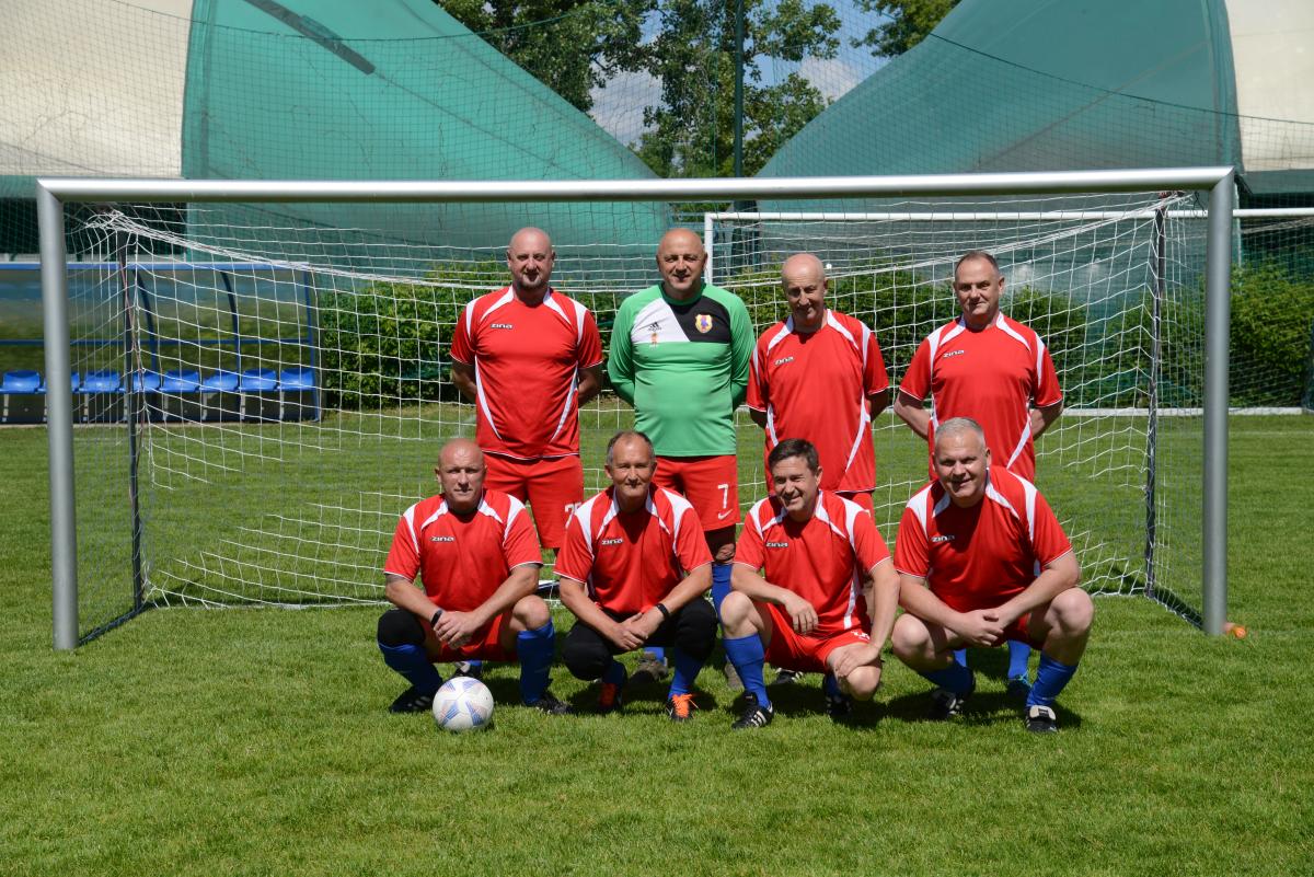 Zdjęcie nr: 7-DSC_3233 Oldboye przedstawia skład męskiej drużyny piłkarskiej, składającej się z ośmiu zawodników, na tle bramki piłkarskiej, na murawie. Siedmiu z nich ubranych jest strój piłkarski koloru czerwonego a jeden w strój bramkarski koloru zielonoczerwonego. Czterech mężczyzn stoi, pozostali spoczywają (kucają) na trawie.