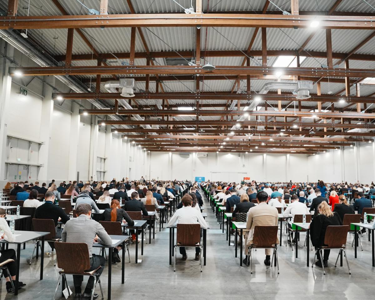 na zdjęciu widać salę, na krzesłach siedzą mężczyźni i kobiety, którzy są uczestnikami konkursu naboru na aplikację.